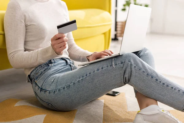 Обрізаний вид молодої жінки, що тримає кредитну картку і використовує ноутбук на підлозі у вітальні — стокове фото