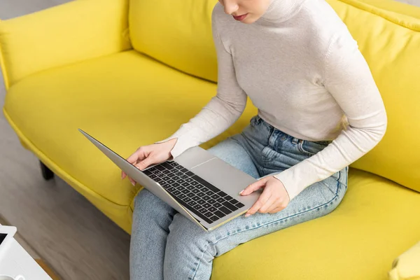 Обрізаний вид молодої дівчини, що використовує ноутбук на дивані у вітальні — стокове фото