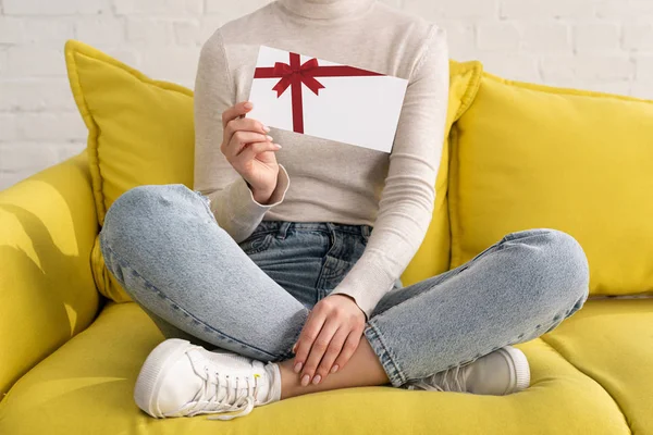 Vista recortada de la niña que muestra la tarjeta de regalo con espacio de copia en el sofá - foto de stock