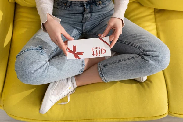 Обрезанный вид девушки с подарочной карточкой на диване — стоковое фото
