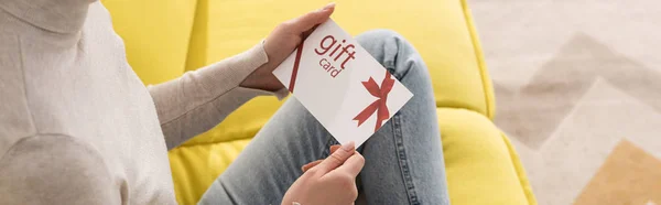 Cropped view of young woman holding gift card on sofa, panoramic shot — Stock Photo