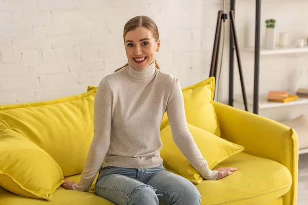 Красива дівчина сидить на дивані у вітальні і посміхається на камеру — стокове фото
