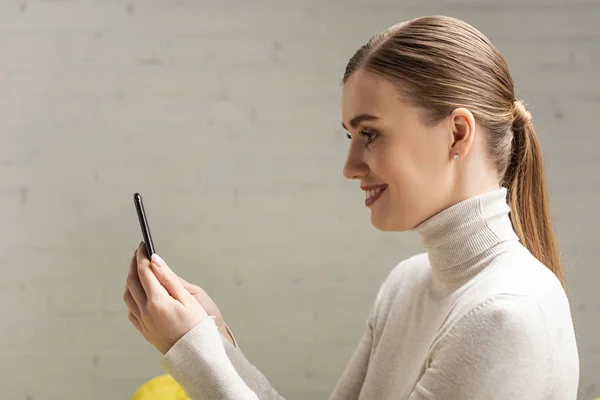 Side view of beautiful smiling girl holding smartphone — Stock Photo