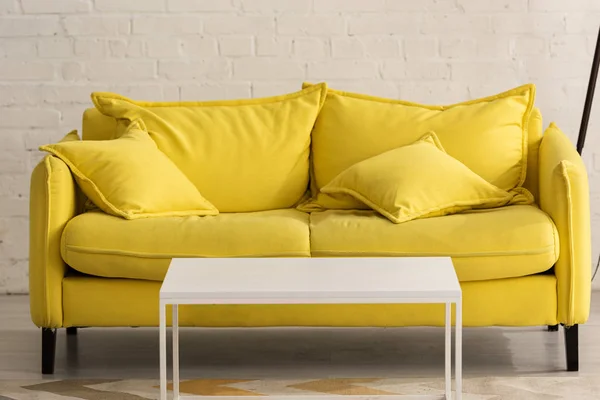 Жовтий диван з подушками і білий кавовий столик у вітальні. — стокове фото