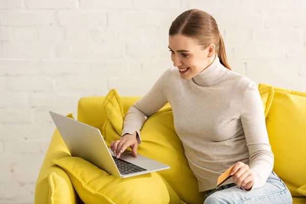Schöne lächelnde Frau mit Kreditkarte mit Laptop auf dem Sofa — Stockfoto