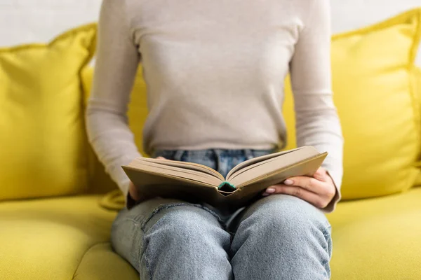 Vista cortada de mulher lendo livro no sofá em casa — Fotografia de Stock