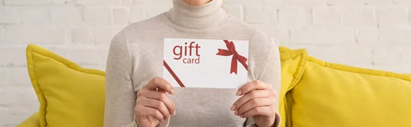 Cropped view of young woman showing gift card on sofa, panoramic shot — Stock Photo