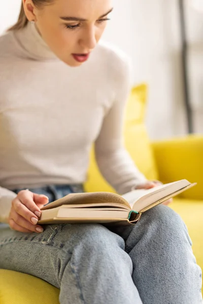 Jovem excitada lendo livro no sofá na sala de estar — Fotografia de Stock