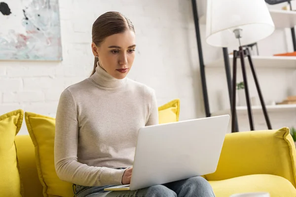 Attraente giovane donna che utilizza il computer portatile sul divano a casa — Foto stock