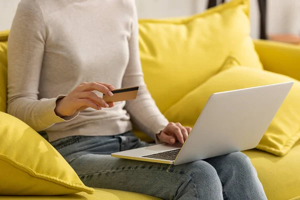 Обрізаний вид дівчини, що тримає кредитну картку і використовує ноутбук на дивані — стокове фото