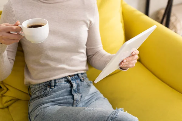 Abgeschnittene Ansicht einer Frau, die Kaffee trinkt und ein digitales Tablet auf der Couch hält — Stockfoto