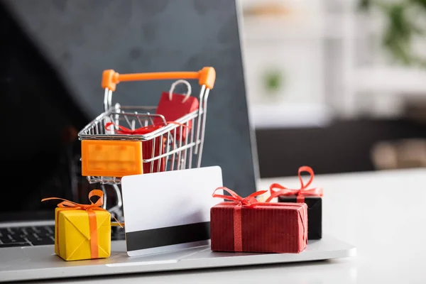 Selective focus of toy cart and gift boxes with credit card on laptop on table — Stock Photo