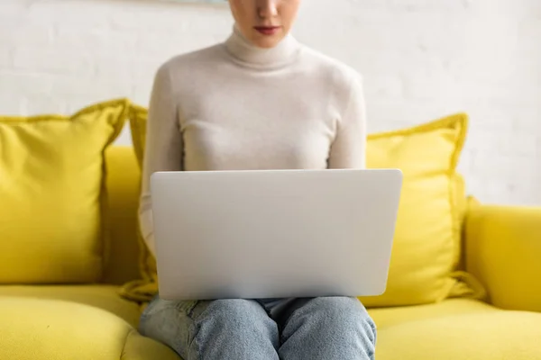 Vista recortada de la mujer joven usando el ordenador portátil en el sofá en casa - foto de stock