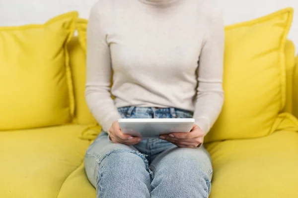 Vista ritagliata della donna che tiene tablet digitale sul divano — Foto stock