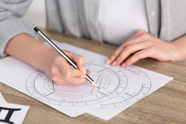 Cropped view of astrologer drawing natal chart on wooden table — Stock Photo