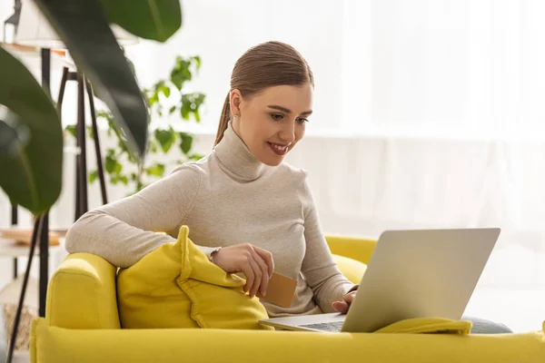 Chica sonriente con tarjeta de crédito y portátil en el sofá en casa — Stock Photo