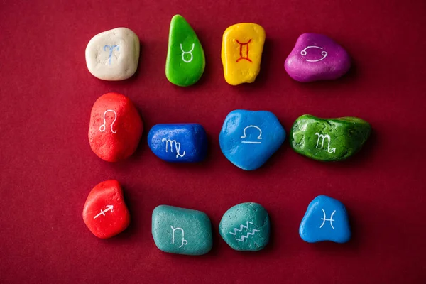 Верхний вид разноцветных камней с знаками зодиака на красной поверхности — стоковое фото