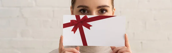 Panoramaaufnahme einer Frau, die ihr Gesicht mit einer Geschenkkarte bedeckt und in die Kamera blickt — Stockfoto