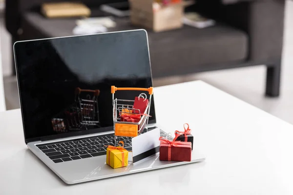 Cajas de regalo de juguete y tarjeta de crédito en el ordenador portátil con pantalla en blanco en la mesa - foto de stock