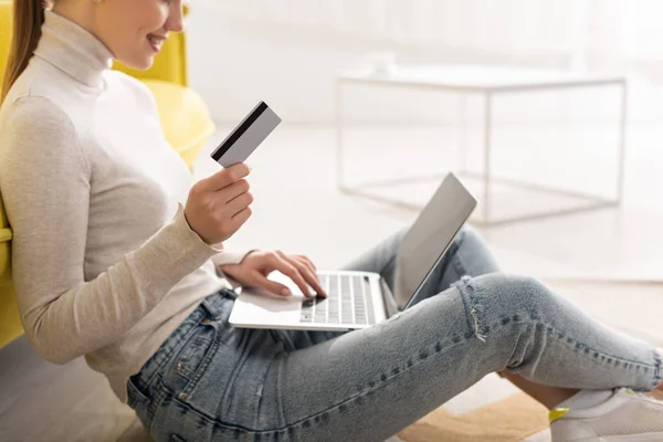 Cropped view of smiling woman holding credit card and using laptop on floor at home — Stock Photo