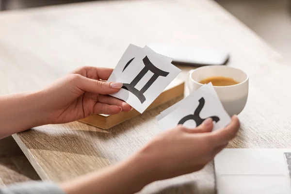 Vista cortada de astrólogo segurando cartões com signos do zodíaco ao lado de café e livro na mesa — Fotografia de Stock