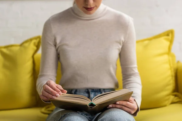 Ausgeschnittene Ansicht einer Frau, die zu Hause auf der Couch Buch liest — Stockfoto