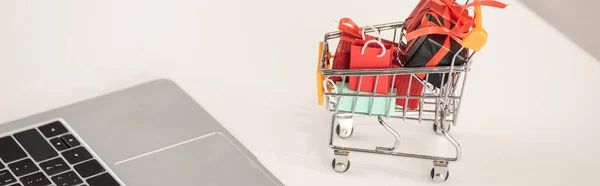 Toy gift boxes in cart beside laptop on table, panoramic shot — Stock Photo