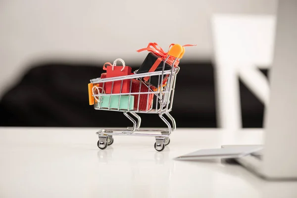 Selective focus of gifts in toy cart beside credit card and laptop on table — Stock Photo