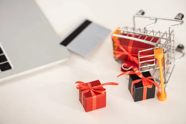 Selective focus of gifts with toy cart beside credit card and laptop on table — Stock Photo