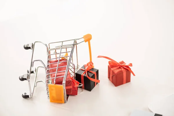 Toy cart with gift boxes beside laptop and credit card on white surface — Stock Photo