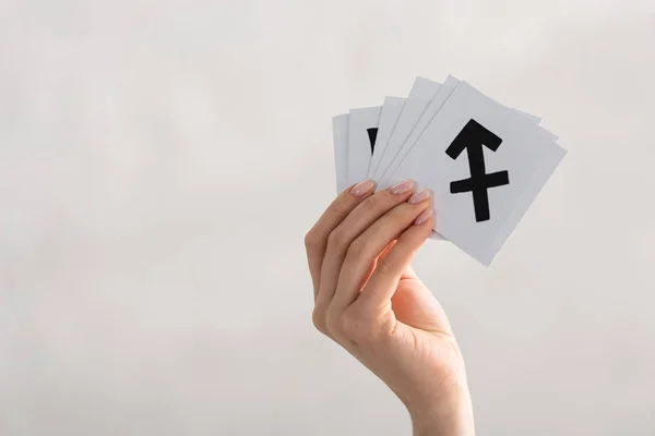 Vista recortada de la mujer sosteniendo tarjetas con signos del zodíaco aislados en gris - foto de stock