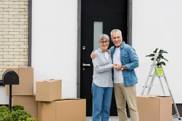 Smiling mature man and woman hugging near new house — Stock Photo