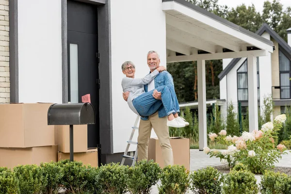 Älterer Mann hält lächelnde Frau in Brille in der Nähe von neuem Haus — Stockfoto