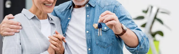 Plano panorámico de hombre maduro sosteniendo las llaves de la nueva casa y la mujer sonriente mirándola - foto de stock