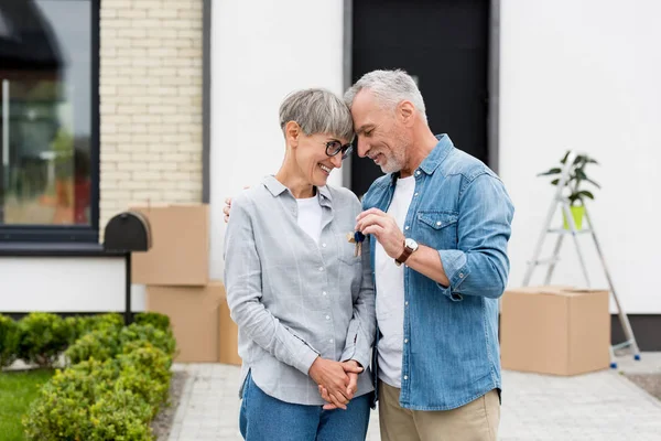 Älterer Mann hält Schlüssel für neues Haus und umarmt lächelnde Frau — Stockfoto