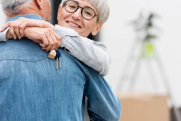 Cropped view of smiling woman holding keys of new house and hugging mature man — Stock Photo