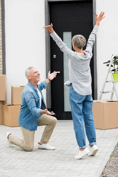 Homme mature pointant vers l'intérieur avec la main et tenant les clés de la nouvelle maison à la femme avec les mains tendues — Photo de stock