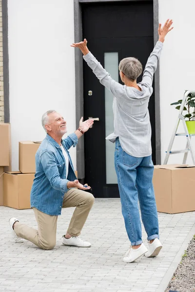 Mature man pointing in with hand and holding keys of new house to woman with outstretched hands — Stock Photo