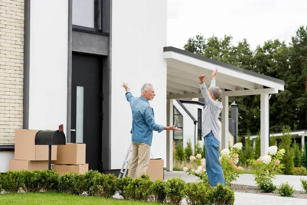 Mature man pointing in with hand and holding keys of new house to woman with outstretched hands — Stock Photo