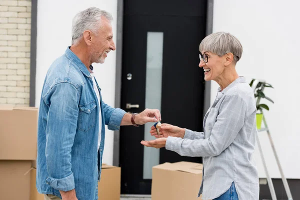 Вид сбоку зрелого мужчины, дающего ключи от нового дома улыбающейся женщине — стоковое фото