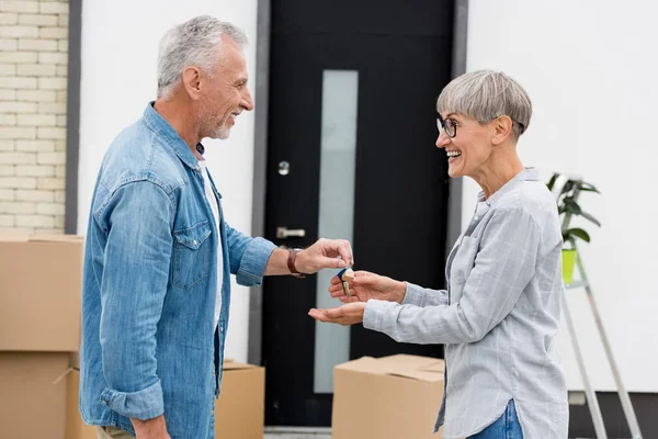 Vista laterale di uomo maturo dando chiavi di nuova casa alla donna sorridente — Foto stock