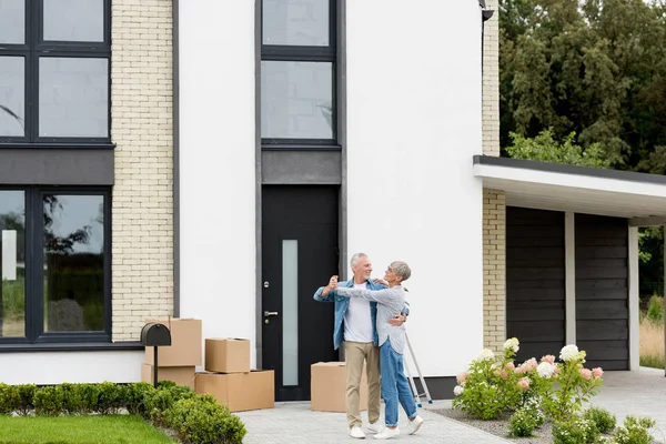Mature man and smiling woman dancing and looking at each other near new house — Stock Photo