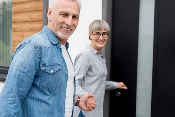 Sonriente mujer cogida de la mano con el hombre y entrar a nueva casa - foto de stock