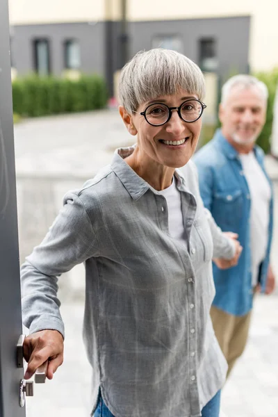 Selective focus of smiling woman holding hands with man and entering to new house — Stock Photo