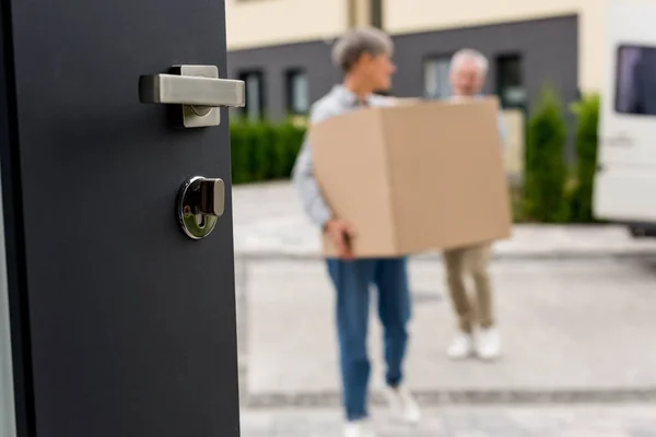 Foyer sélectif de la porte et de l'homme et de la femme mûrs apportant des boîtes à la nouvelle maison sur fond — Photo de stock