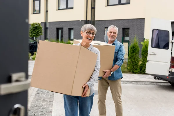 Reifer Mann und lächelnde Frau bringen Kisten ins neue Haus — Stockfoto