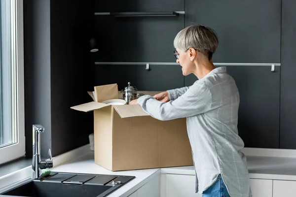 Mature woman in glasses unpacking box in new house — Stock Photo