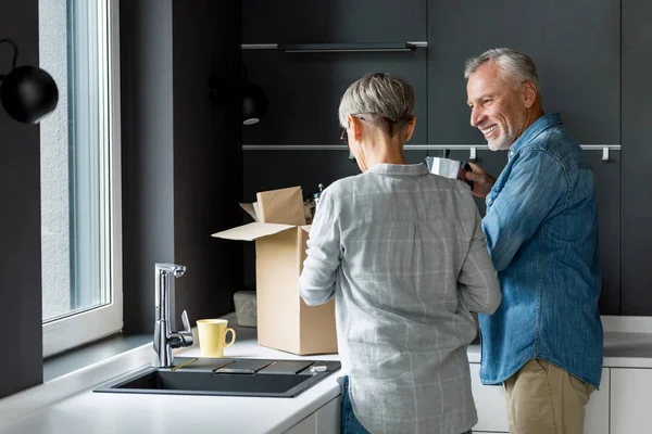 Homme et femme souriant boîte de déballage dans une nouvelle maison — Photo de stock