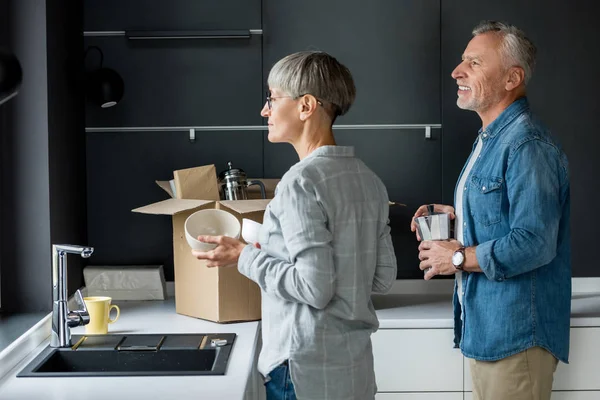 Mature man and woman unpacking box in new house — Stock Photo