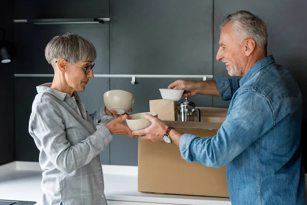 Smiling man and mature woman unpacking box in new house — Stock Photo